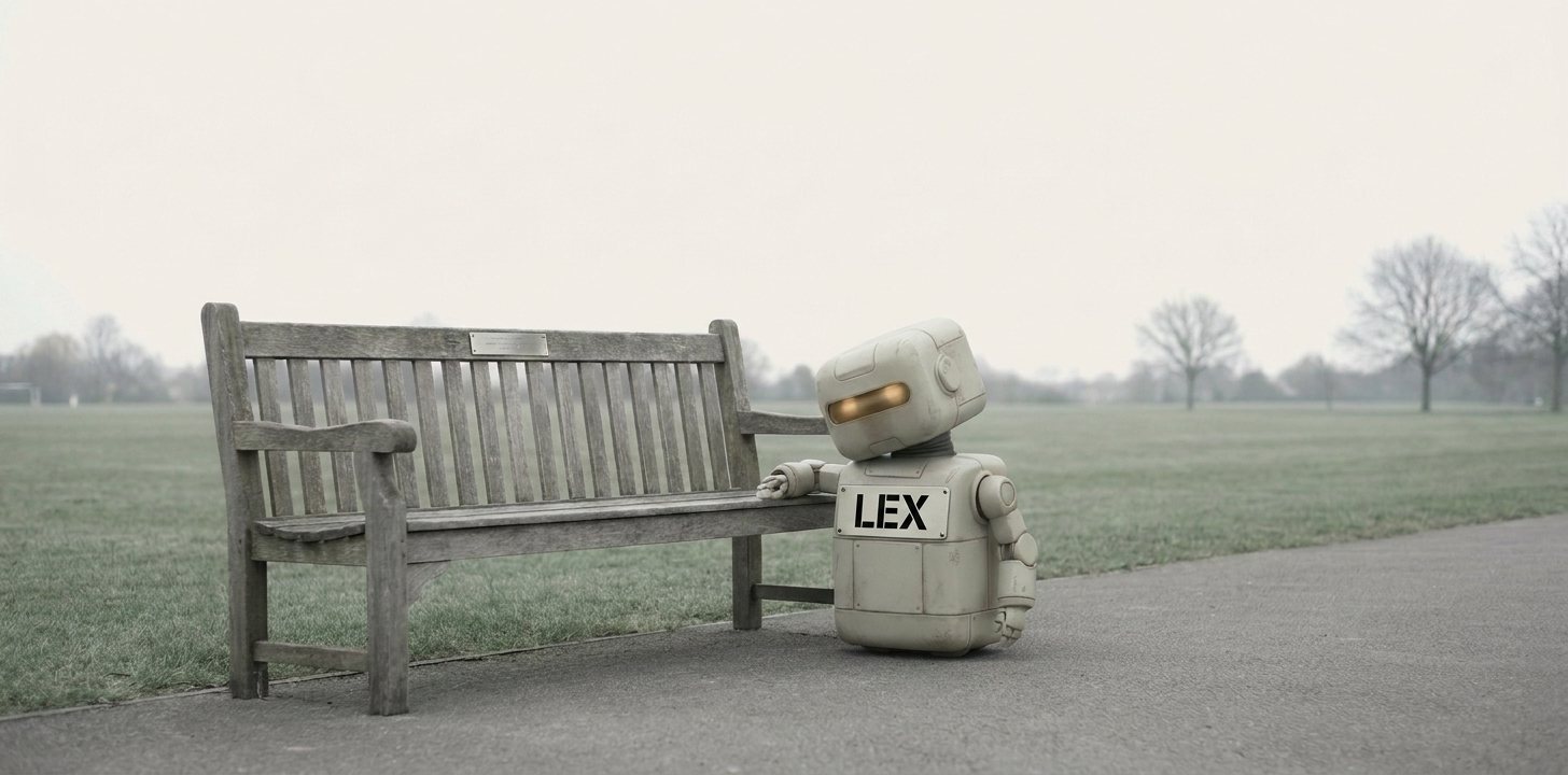 Lex, a small robot with a large LEX name plate across his front, stands on a path in an empty public park with one hand on the arm of a weathered wooden bench, leaning toward the small engraved memorial plaque fixed to its backrest.